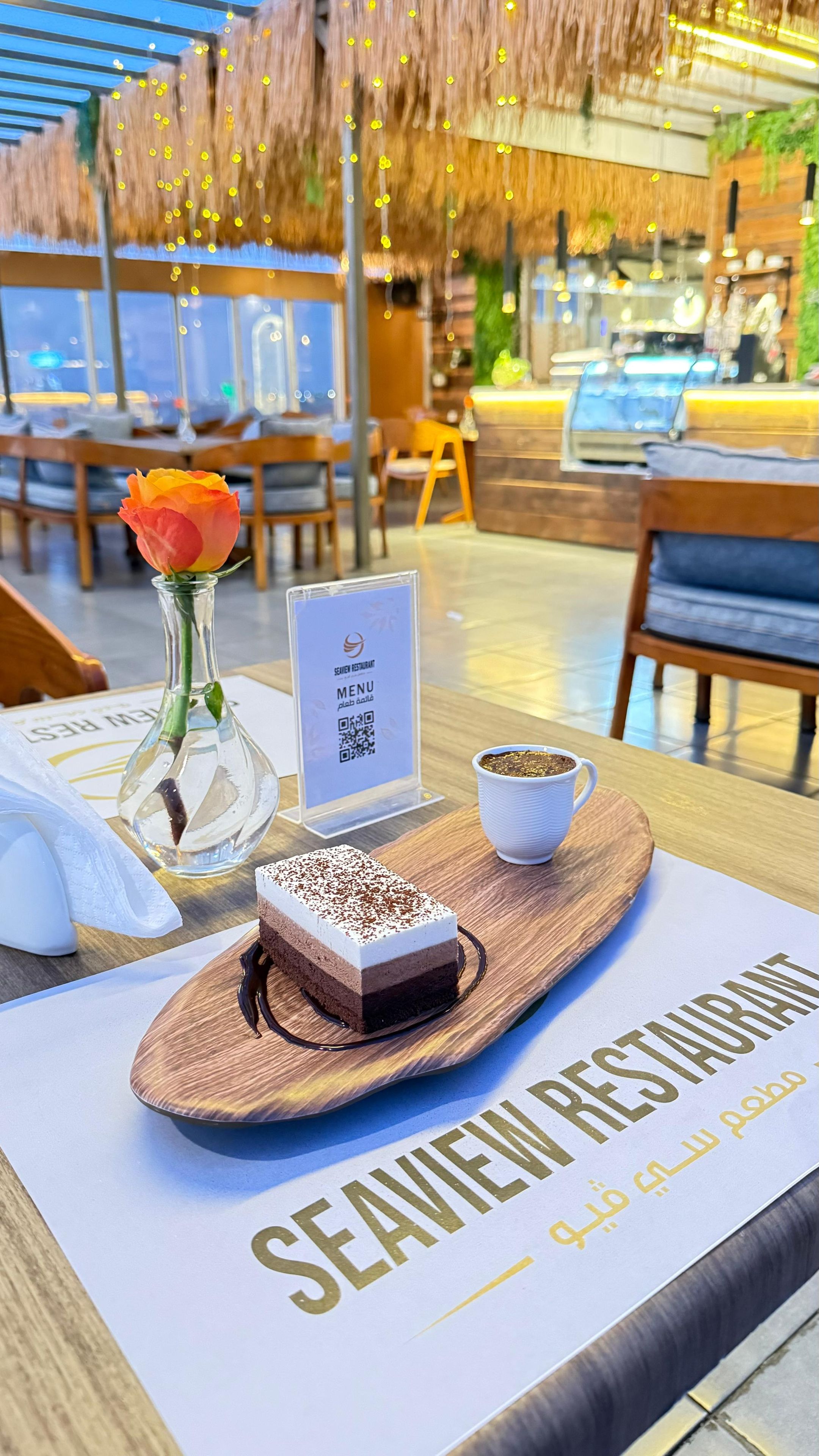A restaurant setting with a dessert on a tray, a menu stand, and a rose in a glass vase.