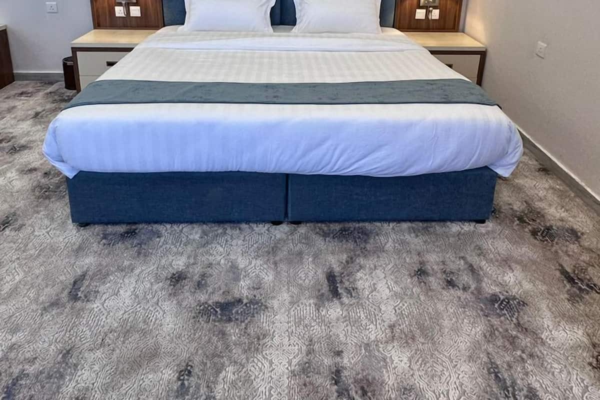 A modern bedroom with a large bed, a built-in headboard, an air conditioning unit, and a carpeted floor.
