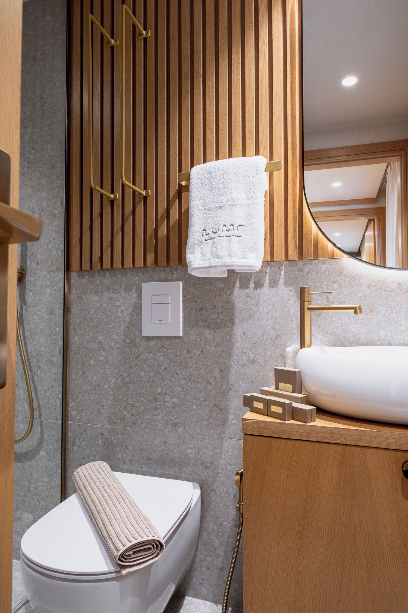 A modern bathroom with a wooden vanity, a white sink, and a toilet with a towel on it.