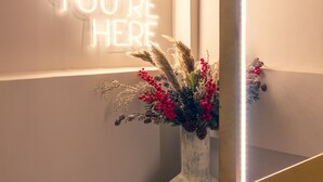 A room with a neon sign reading "SO GLAD YOU'RE HERE" and a rustic vase with dried plants and berries. - Num Suites & Lofts Athens (Athens)