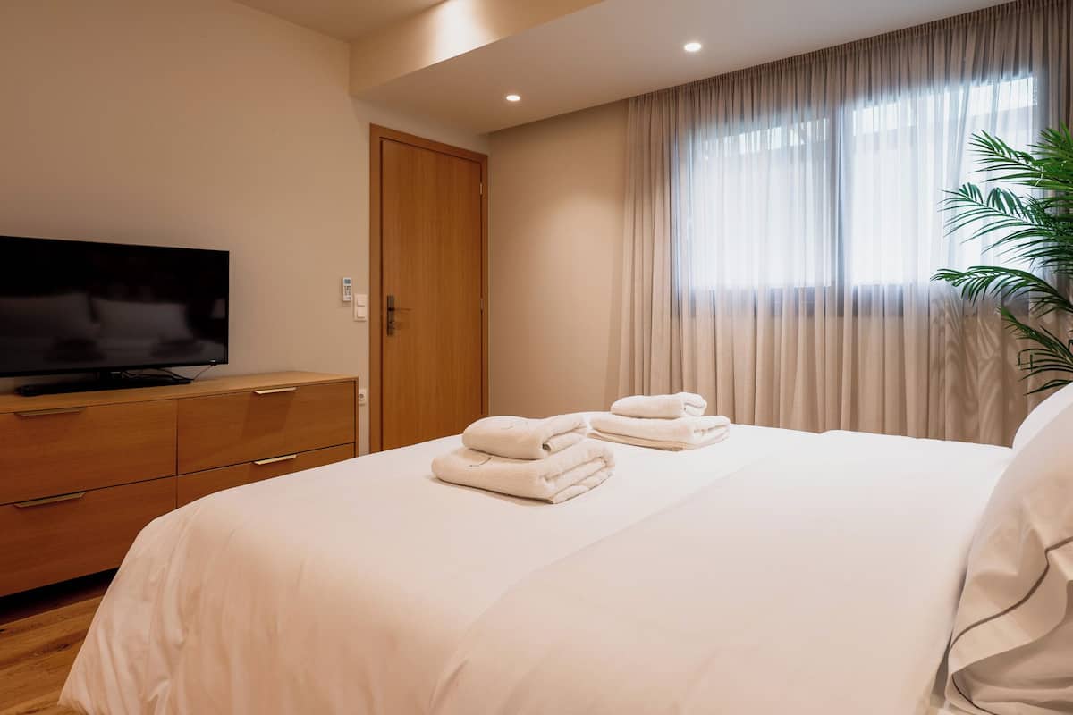 A hotel room with a bed, a TV on a wooden dresser, and a window with curtains.