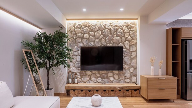 A modern living room with a stone wall, a flat-screen TV, a white sofa, a marble coffee table, and a wooden cabinet. - Num Suites & Lofts Athens (Athens)