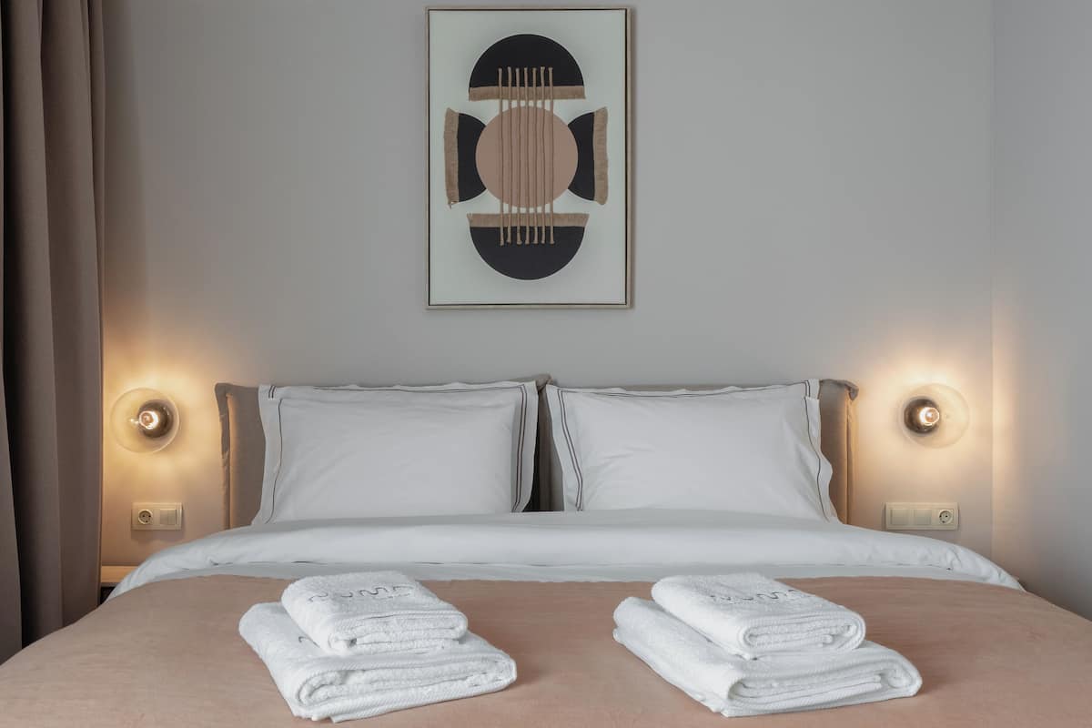 A neatly made bed with two pillows, a framed artwork above, and two wall-mounted lights on either side.