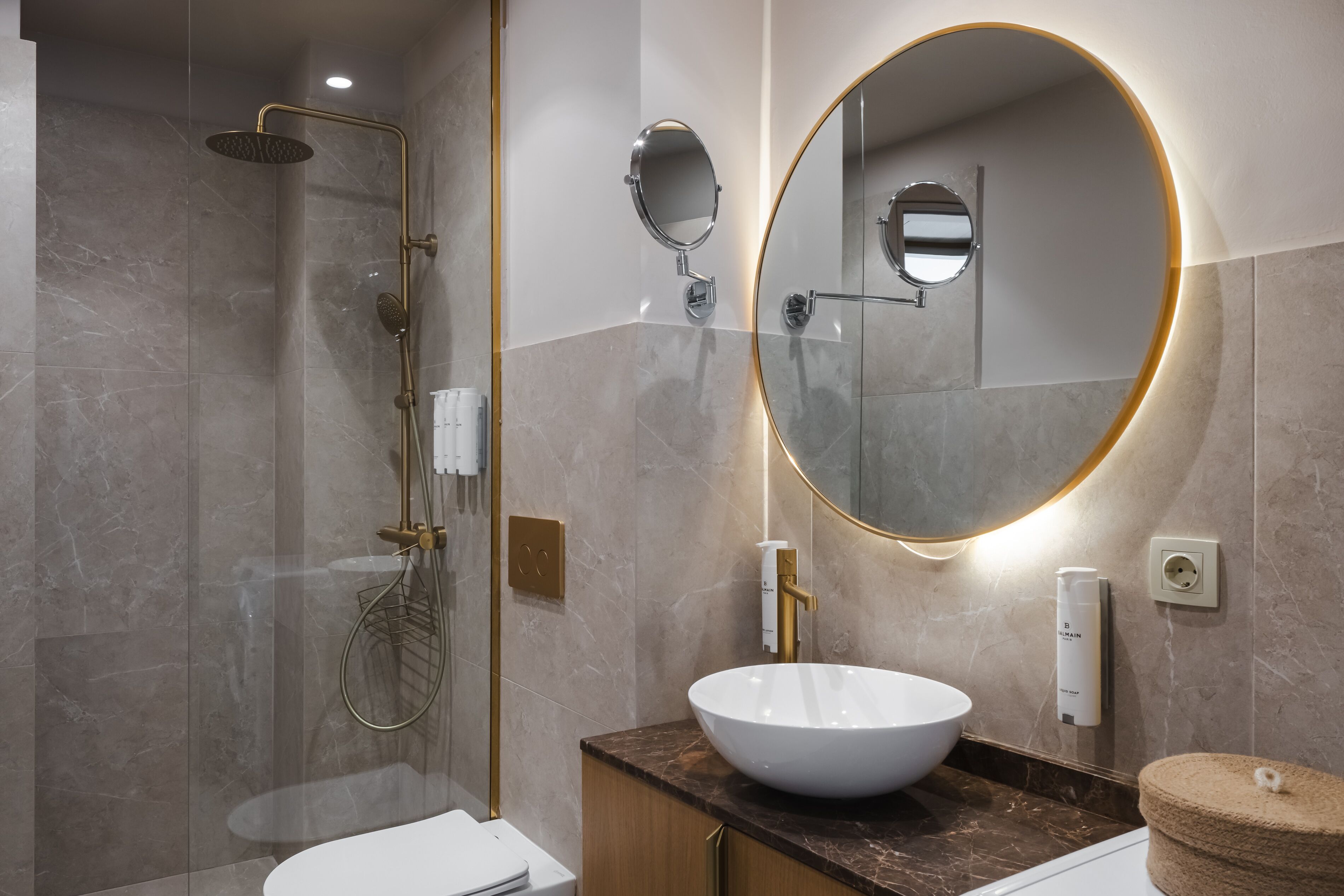 Un baño moderno con un espejo ovalado grande, un lavabo de cerámica blanco, un cabezal de ducha manual y un perchero.