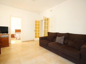 Ein Wohnzimmer mit einem braunen Sofa, einem Fernseher auf einem Holzboden und einem Bett mit einer rosa Decke.