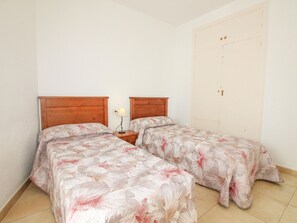 A bedroom with two beds, a nightstand with a lamp, and a white door.