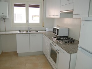 A compact kitchen with a gas stove, microwave, sink, and a window with blinds.