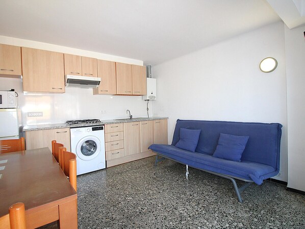 A compact kitchen with a washing machine, a dining table with chairs, and a blue sofa.