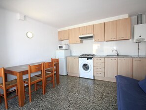 A compact kitchen with wooden cabinets, a washing machine, a microwave, and a dining area with a table and chairs.