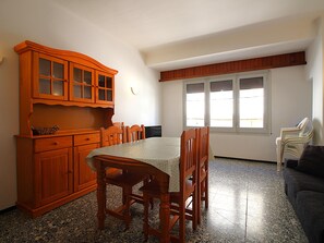 A dining area with a wooden table and chairs, a cabinet with glass doors, and a window with blinds. - Bright Apartment Near Puerto Beach, 2 Double Beds, 1 Single Bed, Newly Renovated, WiFi (Llançà)