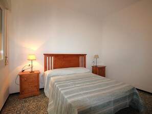 Une chambre à coucher avec un lit en bois, deux tables de chevet avec des lampes, un sol recouvert d’une moquette et une fenêtre avec des rideaux.