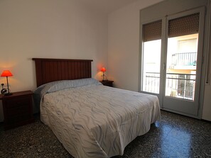 A bedroom with a bed, two bedside tables with lamps, a window with a view, and a door.