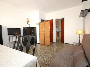 Ein Hotelzimmer mit Fernseher, einem kleinen Tisch, einer Sitzecke und einer Tür zu einer Küchenzeile.