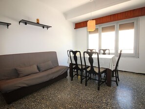 A living room with a sofa, dining table, chairs, and a window with blinds.