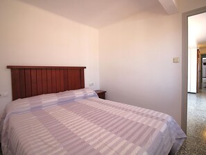 Une chambre à coucher avec une tête de lit en bois, un lit recouvert d’une couvre-lit à rayures, une table de chevet et une porte donnant sur une autre pièce.