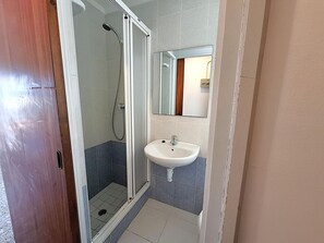 A bathroom with a shower enclosure, a sink, and a mirror.