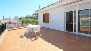A terrace with a table and chairs, a sliding glass door, and a view of buildings in the distance. - Penthouse avec Grande Terrasse, à 100 m de la Plage de Llançà, Rénové, avec WIFI en Été (Llançà)