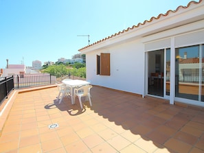 A terrace with a table and chairs, a sliding glass door, and a view of buildings in the distance.