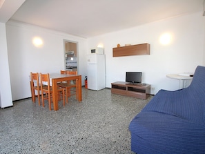 A compact living space with a kitchenette, a dining area, a television, and a sofa.