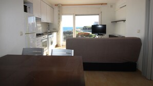 Um espaço de estar compacto com cozinha compacta, televisão de tela plana e vista para o mar.