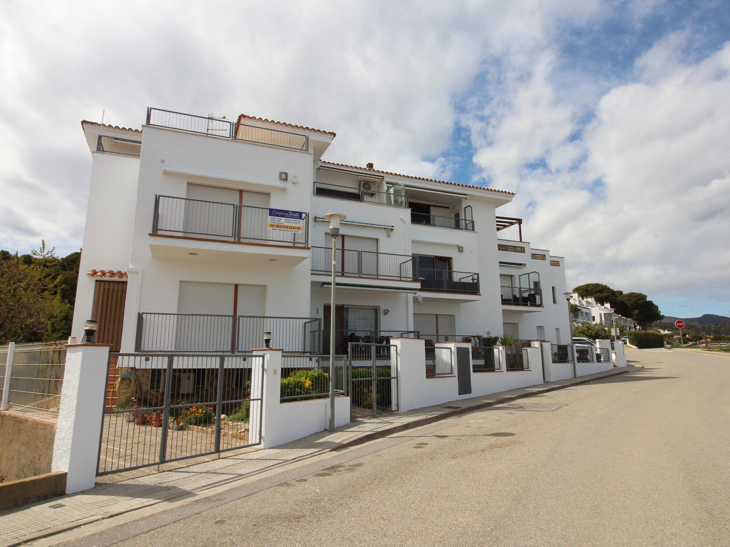 A multi-story residential building with balconies, a gated entrance, and a clear sky.