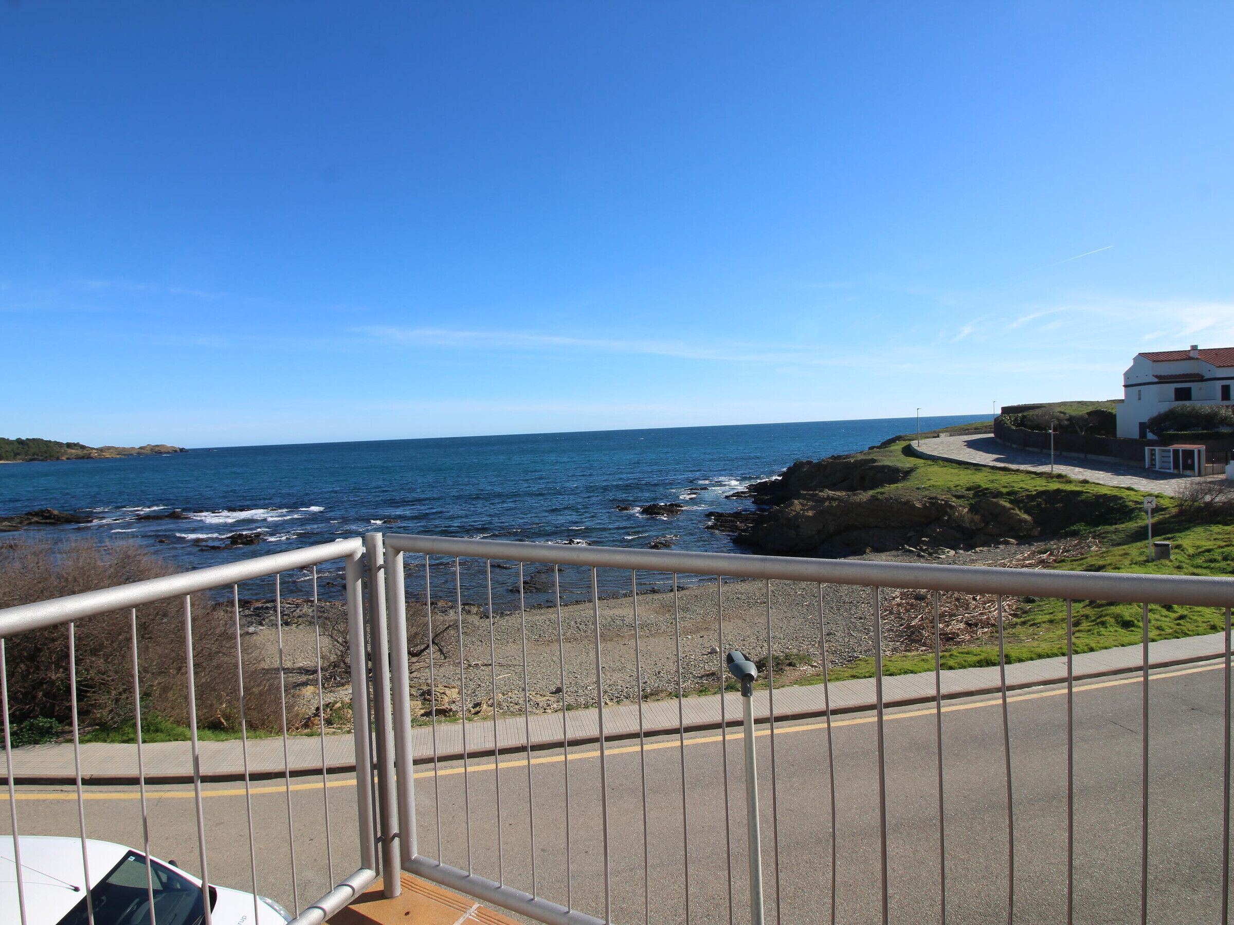 A coastal road with a metal railing, a white building with a red roof, and the ocean in the background.