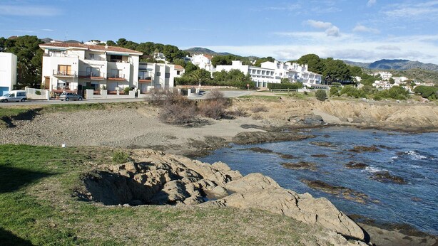 Uma área residencial costeira com edifícios brancos modernos, uma orla rochosa e um céu azul límpido.