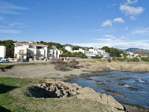 A coastal residential area with modern white buildings, a rocky shoreline, and a clear blue sky.