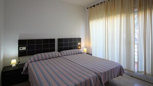 Una cama doble con ropa de cama a rayas, cabecero negro, lámparas de noche y una ventana con cortinas.