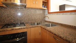 Una cocina con encimeras de granito, un lavamanos de acero inoxidable, armarios de madera, una estufa y un horno.