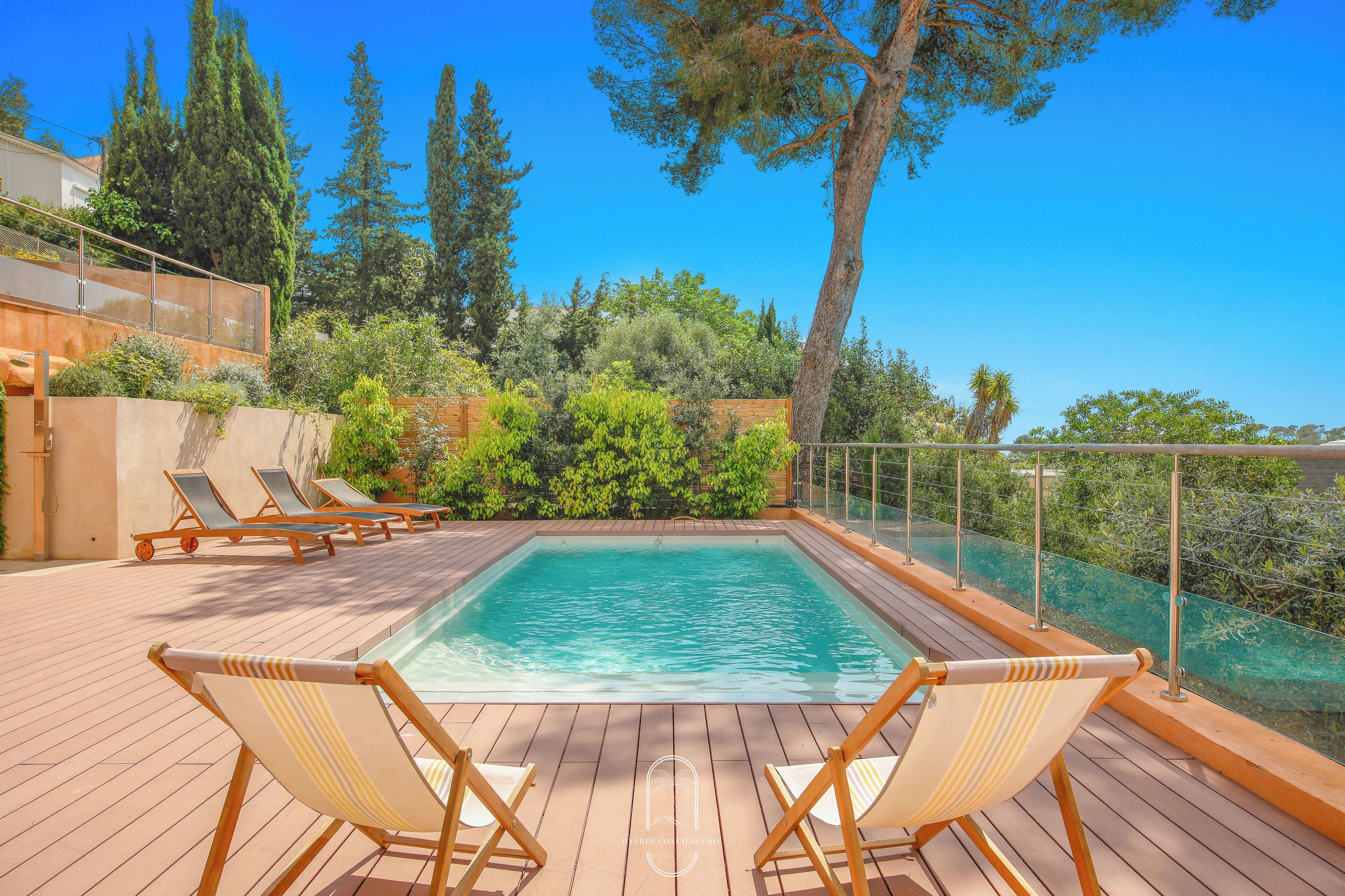 A swimming pool with lounge chairs, surrounded by greenery and trees.