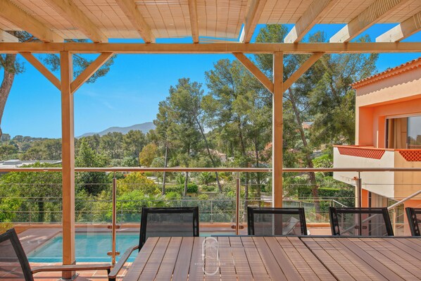 A covered outdoor area with a pool, wooden deck, and chairs.