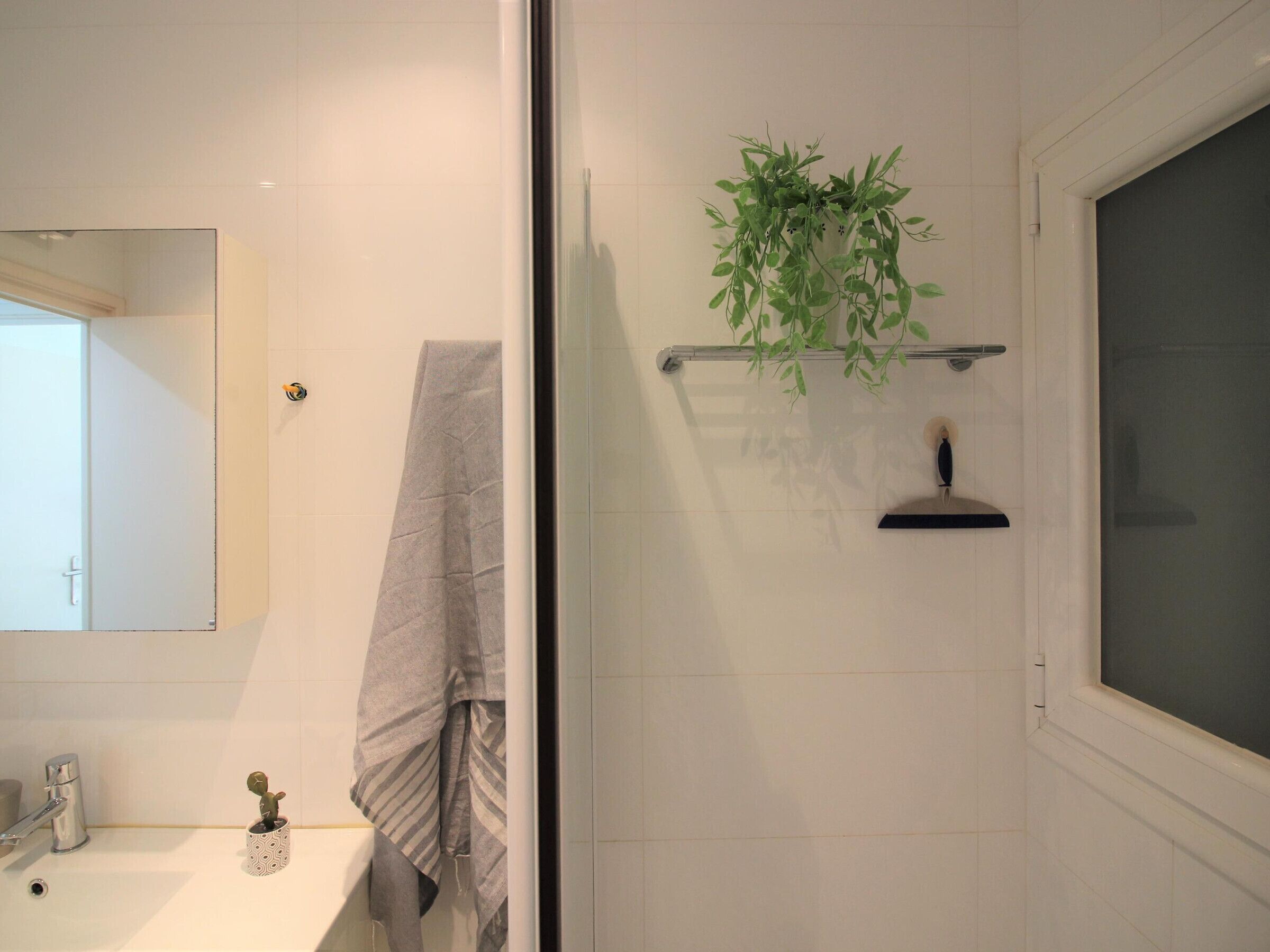 A bathroom with a white sink, a mirror, a towel, a shower area, and a plant on a shelf.