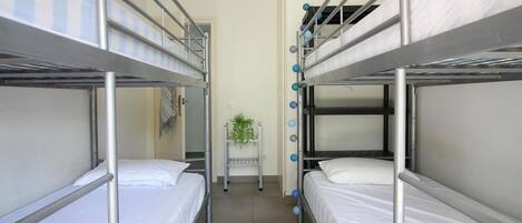 A dormitory room with bunk beds, a small table with a plant, and a door in the background.