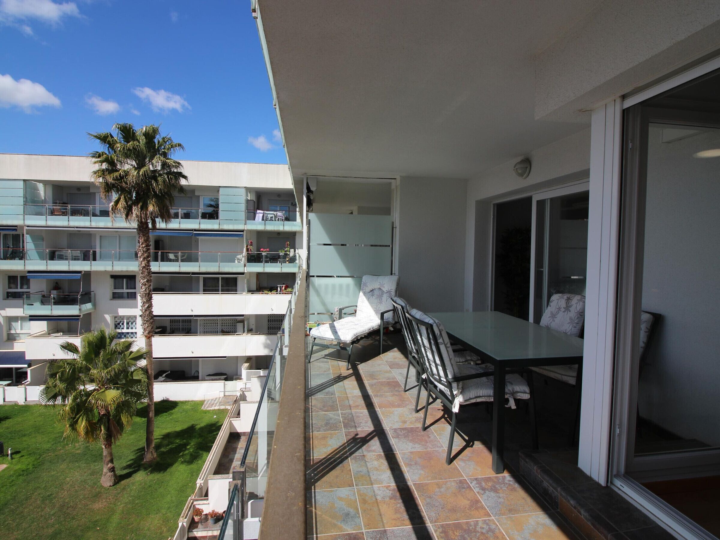 A balcony with a dining table and chairs, overlooking a multi-story building with balconies.