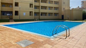 En swimmingpool med flisegulv, omgivet af en bygning med flere etager og altaner.