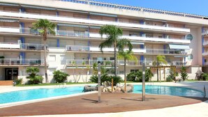 Ein mehrstöckiges Hotel mit Schwimmbad, Palmen und blauem Himmel.