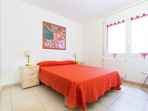 A bedroom with a bed, two bedside tables, a window with pink curtains, a radiator, and a wall-mounted painting.