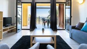 Ein modernes Wohnzimmer mit Flachbildfernseher, einer Couch, einem Couchtisch und einem Balkon mit Meerblick.