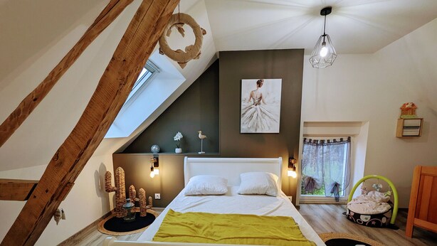 A bedroom with a sloped ceiling, a bed with white bedding, a green throw blanket, a wall-mounted artwork, and a hanging light fixture. - Peaceful Retreat Near ZooParc de Beauval: Modern Comforts, Heated Pool, Nature, and History (Villentrois-Faverolles-en-Berry)