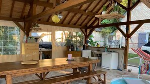 A rustic outdoor kitchen with a wooden table, a bench, and a hammock. - Peaceful Retreat Near ZooParc de Beauval: Modern Comforts, Heated Pool, Nature, and History (Villentrois-Faverolles-en-Berry)