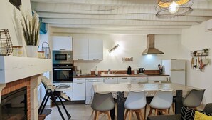 A modern kitchen with white cabinets, a dining table with chairs, a built-in oven, and a hanging light fixture. - Peaceful Retreat Near ZooParc de Beauval: Modern Comforts, Heated Pool, Nature, and History (Villentrois-Faverolles-en-Berry)