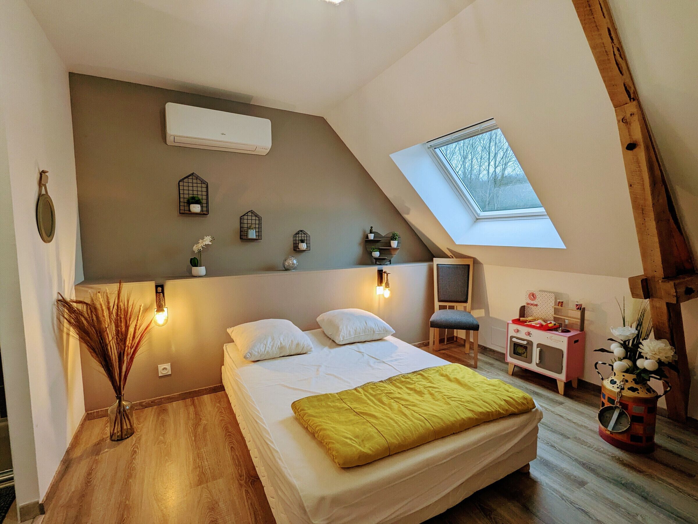 A bedroom with a sloped ceiling, a skylight, a bed with white bedding, a desk with a chair, and decorative wall shelves.