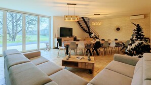 A modern living room with a large window, a staircase, a dining area, and a Christmas tree.