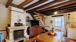A cozy dining area with a fireplace, wooden table, and chairs. A staircase leads to an upper level.