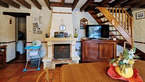A cozy living room with a fireplace, wooden beams, a television, and a dining area.