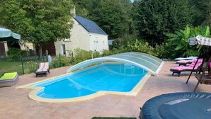 A swimming pool with a glass enclosure, surrounded by a patio area with lounge chairs and a trampoline.