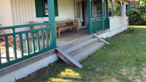 Ein zweistöckiges Haus mit einer Veranda, einer hölzernen Bank und einem kleinen Tisch.