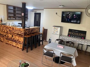 Un restaurant doté d’un bar en bois, de tabourets de bar, d’une table avec des chaises, d’un téléviseur mural et d’une enseigne indiquant « GUESTHOUSE MOCHILERO ».