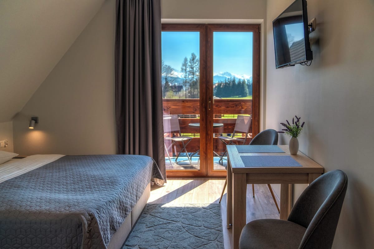 A bedroom with a bed, a desk with a chair, a TV, and a view of a deck with outdoor seating.